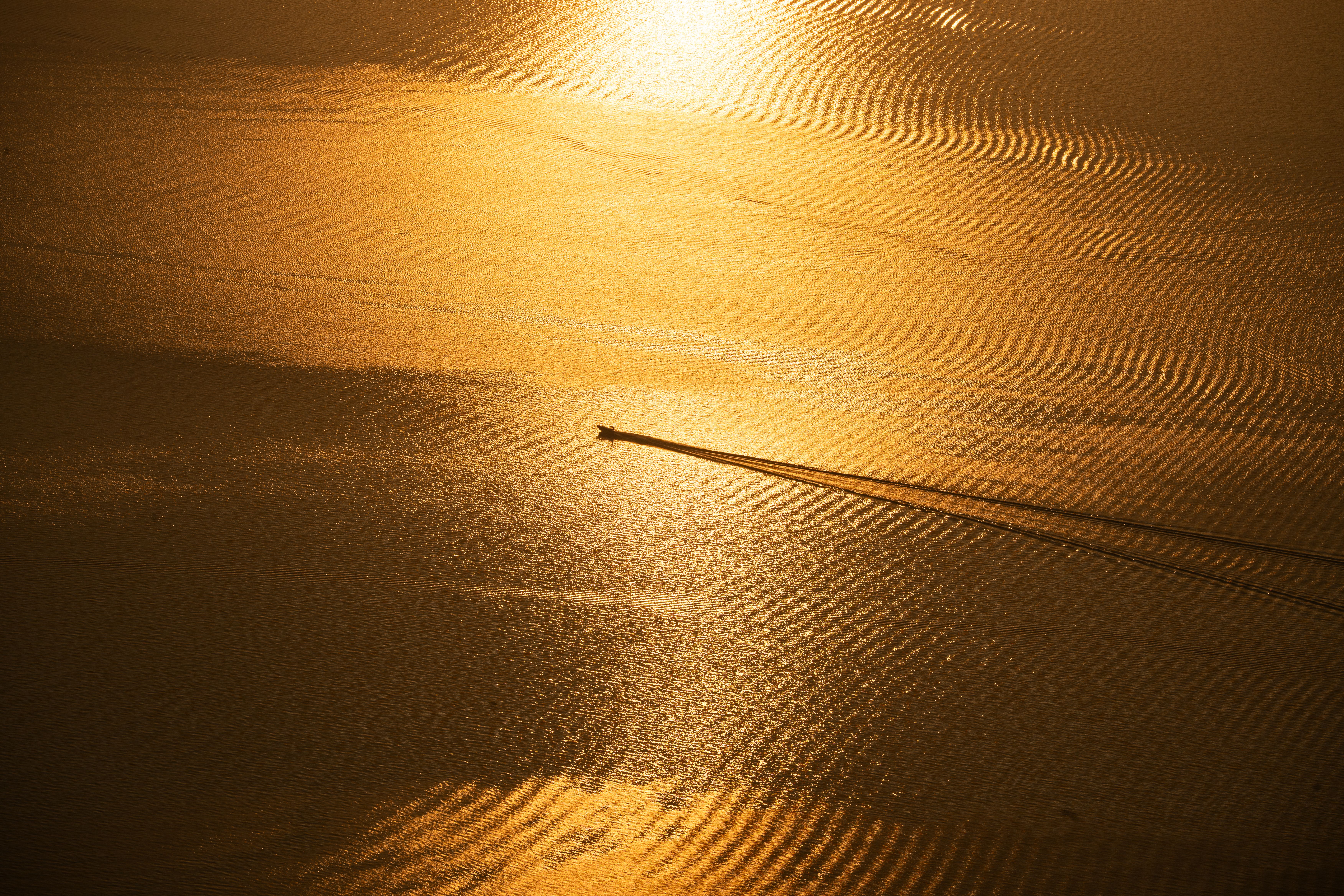Un hors-bord fend une mer dorée au coucher du soleil